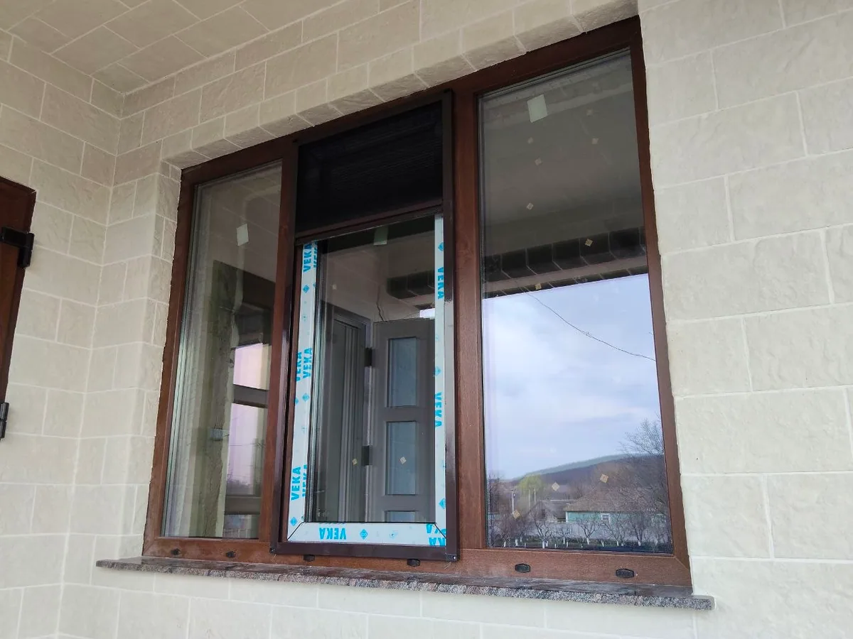 Fereastră termopan cu trei foi, profil PVC laminat maro pe fațadă de piatră