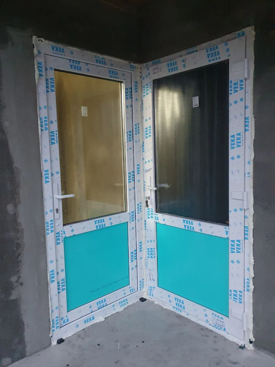 Două uși PVC albe la colț, cu geam termopan sus și panou sandwich jos